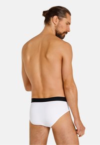 Mutande bianche con un elastico nero, che mostrano una trama di tessuto liscia. Il modello è posizionato di spalle, con la parte superiore del corpo nuda.