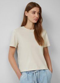 Koszulka z krótkimi rękawami i okrągłym dekoltem w beżowym kolorze, o luźnym kroju i gładkiej strukturze. Połączona z jasnoniebieskimi spodniami o wysokim stanie.