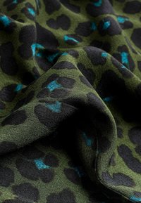 Tissu imprimé léopard avec une base vert olive, présentant des taches noires et des accents bleu sarcelle. Texture douce, drapée avec des plis visibles.