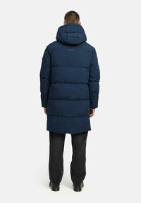 Navy puffy coat with a hood, featuring a quilted design and a straight cut, paired with dark pants and black shoes.