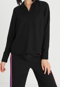 Černý dlouhý rukáv top s výstřihem do V a volným střihem, s jemnou texturou a minimalistickým designem, doplněný černými kalhotami.