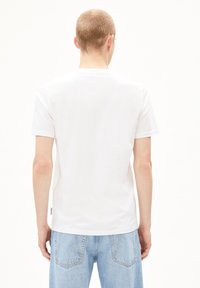 Weißes Baumwoll-T-Shirt mit Rundhalsausschnitt, kurzen Ärmeln und geradem Saum. Verfügt über ein kleines Etikett auf der linken Seite in der Nähe des Saums.