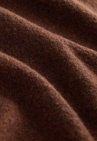 Brauner Wollstoff mit einer weichen, strukturierten Oberfläche, der subtile Farbnuancen und wellenförmige Falten aufweist.