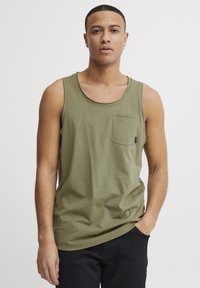 Olivengrünes Tanktop aus leichtem Stoff. Eigenschaften: Rundhalsausschnitt und eine linke Brusttasche mit Etikett, kombiniert mit dunklen Hosen.