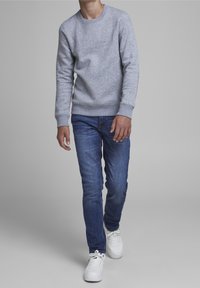 Šedá mikina s kulatým výstřihem, žebrovanými manžetami a lemem, v kombinaci s modrými slim-fit džíny a bílými teniskami.