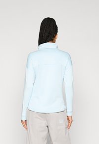 Svetlomodrý fleecový pulover s vysokým golierom, dlhými rukávmi a textúrovaným vzorom. V kombinácii so svetlosivými cargo nohavicami.