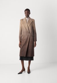 Lange, bruin gradient wolcoat met gekartelde revers, twee voorkeurszakken en een enkele knoopsluiting. Draagt over een nauwsluitende grijze coltrui.