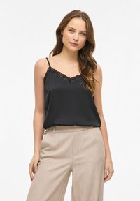 Camisole en satin noir avec bordure en dentelle le long de l'encolure, associée à un pantalon beige clair à jambes larges. Texture lisse ; bretelles spaghetti réglables.