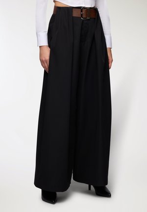 Pantaloni neri a gamba larga in tessuto liscio, con vita alta, pieghe profonde e cintura marrone con fibbia quadrata.