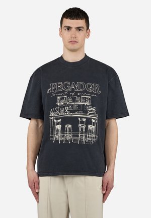 Black oversized T-shirt with white graphic of a bar scene, featuring stylized text "PEGADOR Scent of summer" incorporating minimalist design elements.