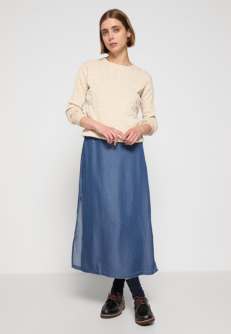 Beige Strickpullover mit Dreiviertelärmeln, kombiniert mit einem fließenden Jeansrock mit Seitenschlitz und schwarzen Schnürschuhen.