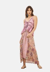 Top de tirantes rosa con volantes combinado con una falda larga estampada que presenta diseños florales y de cachemir en tonos beige y rosa.