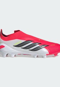 Ροζ και λευκό ποδοσφαιρικό παπούτσι με υφή στην επάνω επιφάνεια, διακοσμημένο με μαύρες ρίγες και λεπτομέρειες. Σχεδιασμός τύπου slip-on με χαμηλό προφίλ και καλουπωμένα καρφιά.