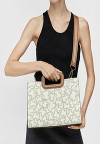 Bolso estructurado con una superficie blanca y un patrón abstracto en gris. Cuenta con un asa superior marrón y una correa de hombro desmontable.