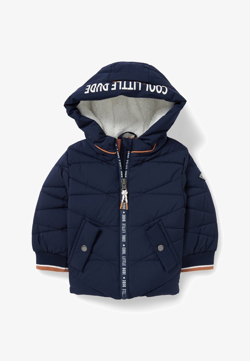 Veste rembourrée marine avec capuche, texture matelassée, doublure en fausse fourrure crème et accents orange. Comprend des poches zippées et à boutons-pression.