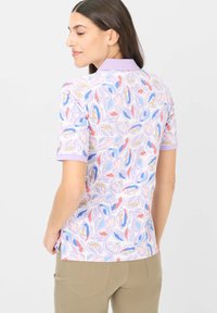 Polo a maniche corte con base lavanda e motivi di foglie colorate. Il colletto e i polsini sono anch'essi lavanda, con spacchi laterali all'orlo.