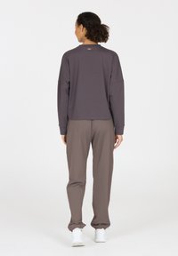 Graues Langarmshirt mit entspannter Passform und lockeren braunen Hosen. Der Stoff wirkt glatt und hat einen dezenten Glanz. Weiße Sneakers runden den Look ab.