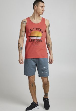 Röd linne med en grafisk solnedgångsdesign; grå shorts med tryckt logotyp; svarta sneakers; avslappnad passform och lättviktigt material.