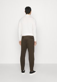 Bruna skräddarsydda byxor med en slät textur och dubbla bakfickor, ihop med en vit långärmad skjorta och svarta sneakers.