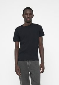 Tricou scurt negru, dintr-un material moale, cu guler rotund și un design minimalist. Asortat cu blugi de denim gri închis.