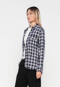 Langsleeve flanellen overhemd in marineblauw en wit ruitpatroon, met een button-down kraag en twee borstzakken, gemaakt van geweven stof.