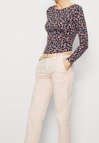 Långärmad topp med svart bas som har ett färgglatt handtrycksmönster. Matchad med ljusrosa byxor och ett vävt bälte.