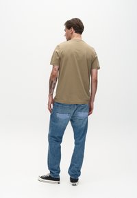 Tricou kaki cu decolteu rotund, asortat cu pantaloni din denim albastru care au buzunare cu petice mai deschise și o siluetă cu picioare drepte.