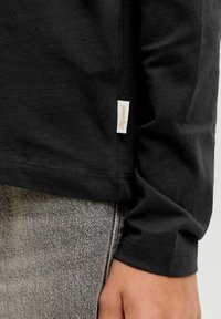 Zwarte lange mouwen shirt met een getailleerd ontwerp. Heeft een zijlabel en een gladde, fijne breistructuur. Gepaard met lichtgrijze denim.