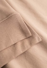 Jasnobeżowa tkanina o miękkiej, teksturowanej powierzchni. Mieszanka bawełny z zagiętym brzegiem i starannie wykonanym przeszyciem.