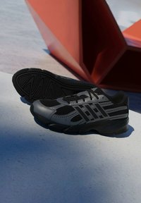 Čierne športové topánky s priedušným zvrškom v šedej farbe, okrúlou špičkou a textúrovanou gumovou podrážkou s jasne definovanými vzormi trakcie.