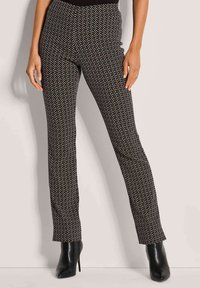 Zwart-wit gestreepte broek met een slim fit, met een geometrisch design. Hoge tailleband en uitlopende broekspijpen. Gecombineerd met zwarte hoge hakken.