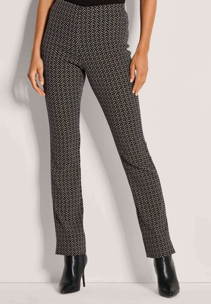 Schwarz-weiße gemusterte Hosen mit slim fit, die ein geometrisches Design aufweisen. Hoher Bund und ausgestelltes Bein. Kombiniert mit schwarzen Absatzstiefeln.