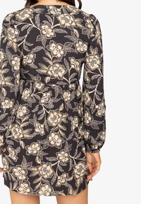 Vestido negro con mangas largas y abullonadas, con un patrón floral en tonos crema y beige. Cintura entallada con una falda fluida.