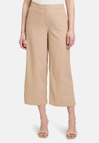 Beige Leinenhose mit weitem Bein und glatter Textur, ausgestattet mit Seitentaschen und einem flachen Bund, kombiniert mit hellen Absatzsandalen.
