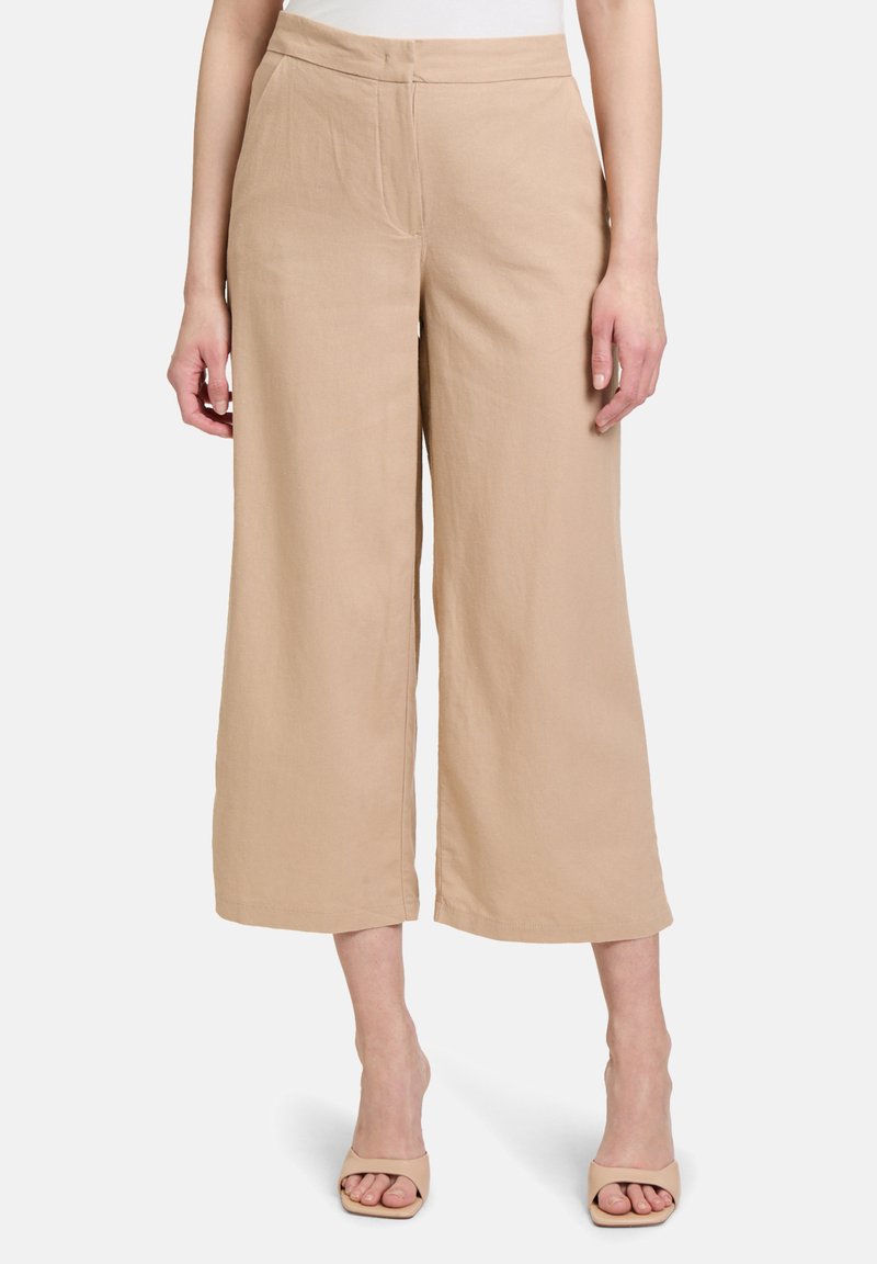 Beige Leinenhose mit weitem Bein und glatter Textur, ausgestattet mit Seitentaschen und einem flachen Bund, kombiniert mit hellen Absatzsandalen.