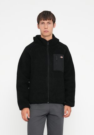 Black fleece jacket with a hood, featuring a zip closure and a left chest pocket in black fabric. The jacket has a soft, textured finish.