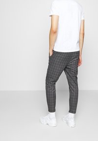 Grå rutiga byxor med smal passform, utrustade med sidofickor och en flexibel midja. Kombinerat med en vit t-shirt och vita sneakers.