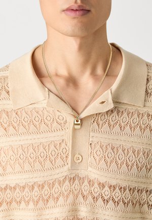 Beige kant polo shirt met een gestructureerd ruitpatroon, voorzien van een kraag en een gouden ketting met een sluitingdetail.