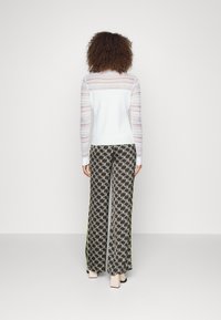 Haut à manches longues bleu clair avec manches rayées transparentes, associé à un pantalon large à motifs géométriques noirs et verts.