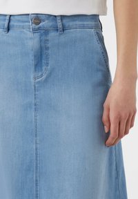 Jupe en denim bleu clair, avec une texture lisse, des poches avant, une fermeture à boutons, et une taille ajustée avec une silhouette légèrement évasée.