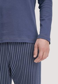 Navyblaues Langarmshirt kombiniert mit navyblauen gestreiften Hosen. Das Shirt hat einen Rundhalsausschnitt, während die Hose vertikale weiße Streifen hat. Weicher Stoff.