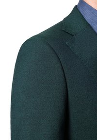 Ciemnozielona marynarka z teksturowanej tkaniny, ostre klapy i dopasowany krój. Zbliżenie na okolicy ramienia, ukazujące szczegóły przeszycia.