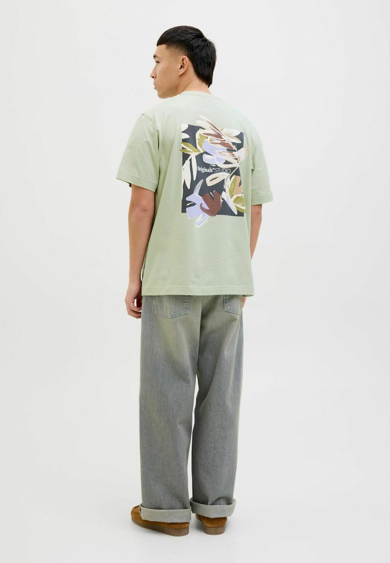 Light green short-sleeve t-shirt with a graphic print on the back, paired with loose gray jeans and brown footwear.