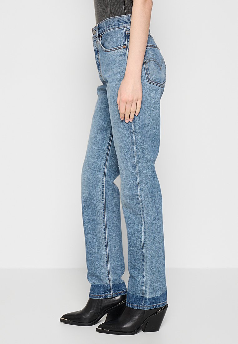 Jeans dritti azzurri in denim, dotati di cinque tasche e vita alta, abbinati a stivali neri con tacco alla caviglia.
