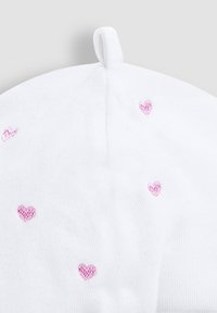 Cappello bianco morbido con piccoli cuori rosa ricamati sparsi sulla superficie e un occhiello in cima per appenderlo.