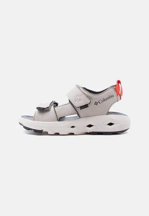 Sandale Columbia gri deschis cu curele reglabile, talpă albă amortizată, crampoane negre și fâșie roșie de tragere la călcâi.
