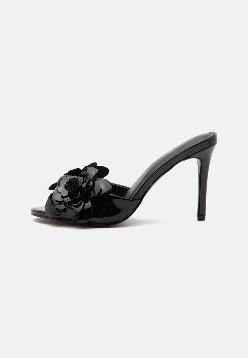 Mule noire en cuir verni à talon haut avec bout ouvert et grande décoration florale sur la bride avant sur fond uni.