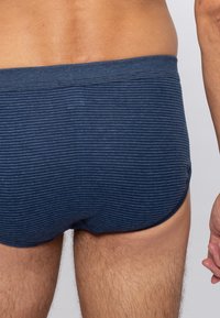 Marineblauwe gestreepte zwembroek met een lage taille, zichtbaar elastische tailleband en een gladde textuur, toont de achterkant en bovenbeen.