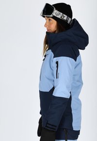 Snow jacket with a dual-tone design: light blue and dark blue sections, featuring a hood, zippers, and an athletic fit. Textured fabric.