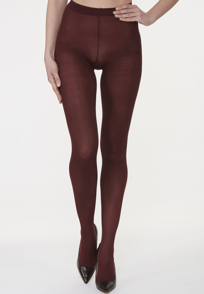 Opake burgunderfarbene Strumpfhosen mit glatter Textur und hohem Bund, getragen mit schwarzen spitzen Absätzen, die eine elegante Beinlinse betonen.